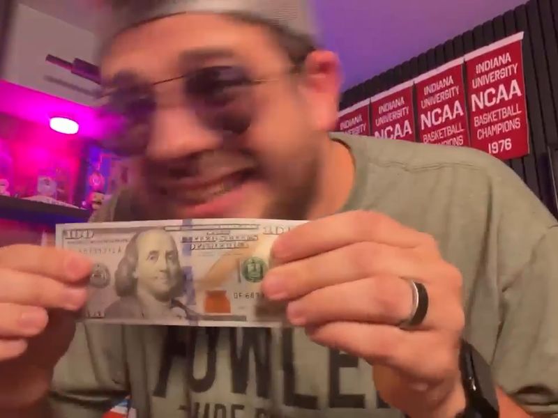 Avery in sunglasses, grinning and holding up a hundred-dollar bill